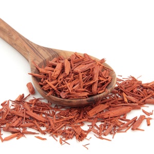 May include: A wooden spoon filled with red sandalwood chips, with more chips scattered around the spoon on a white background.