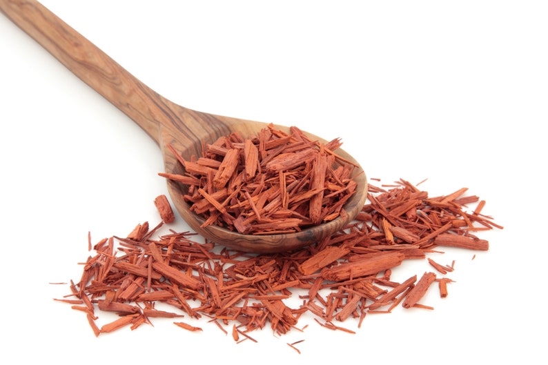 May include: A wooden spoon filled with red sandalwood chips, with more chips scattered around the spoon on a white background.