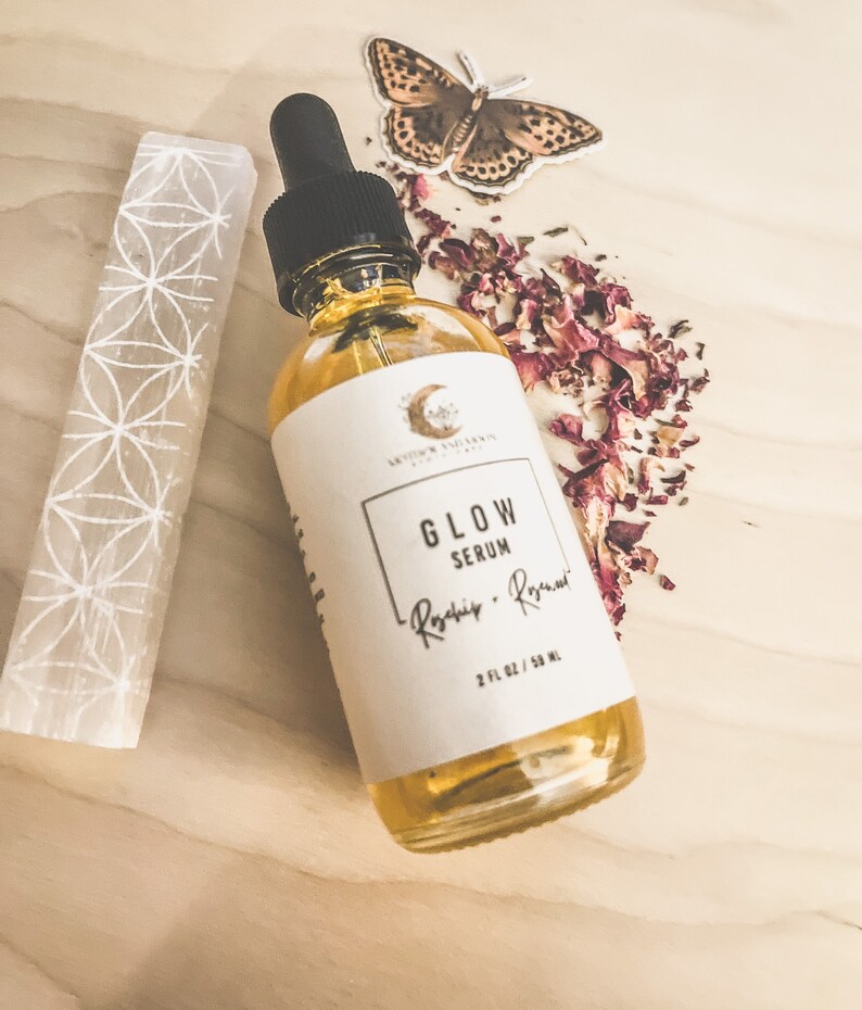 Peut inclure: Un flacon en verre transparent avec une &eacute;tiquette blanche sur laquelle est inscrit "Glow Serum - Rosehip - Rosemar" et "2 fl oz / 50 ml". Le flacon est pos&eacute; sur une surface en bois brun clair avec un cristal blanc et des p&eacute;tales de rose s&eacute;ch&eacute;s.