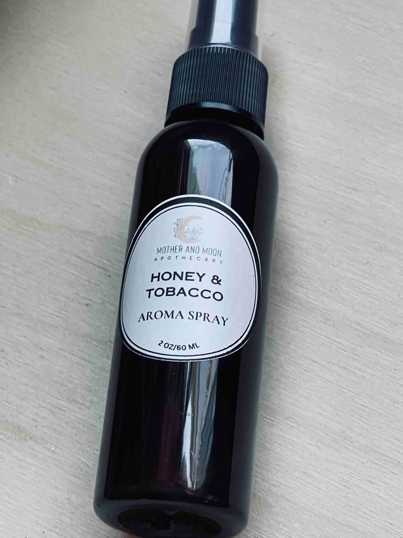 May include: A black glass bottle with a white label that reads "Mother and Moon Apothecary Honey & Tobacco Aroma Spray 2 oz/60 ml".