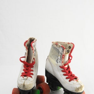 May include: A pair of white roller skates with red laces and green wheels. The skates have a worn look and are on a white background.
