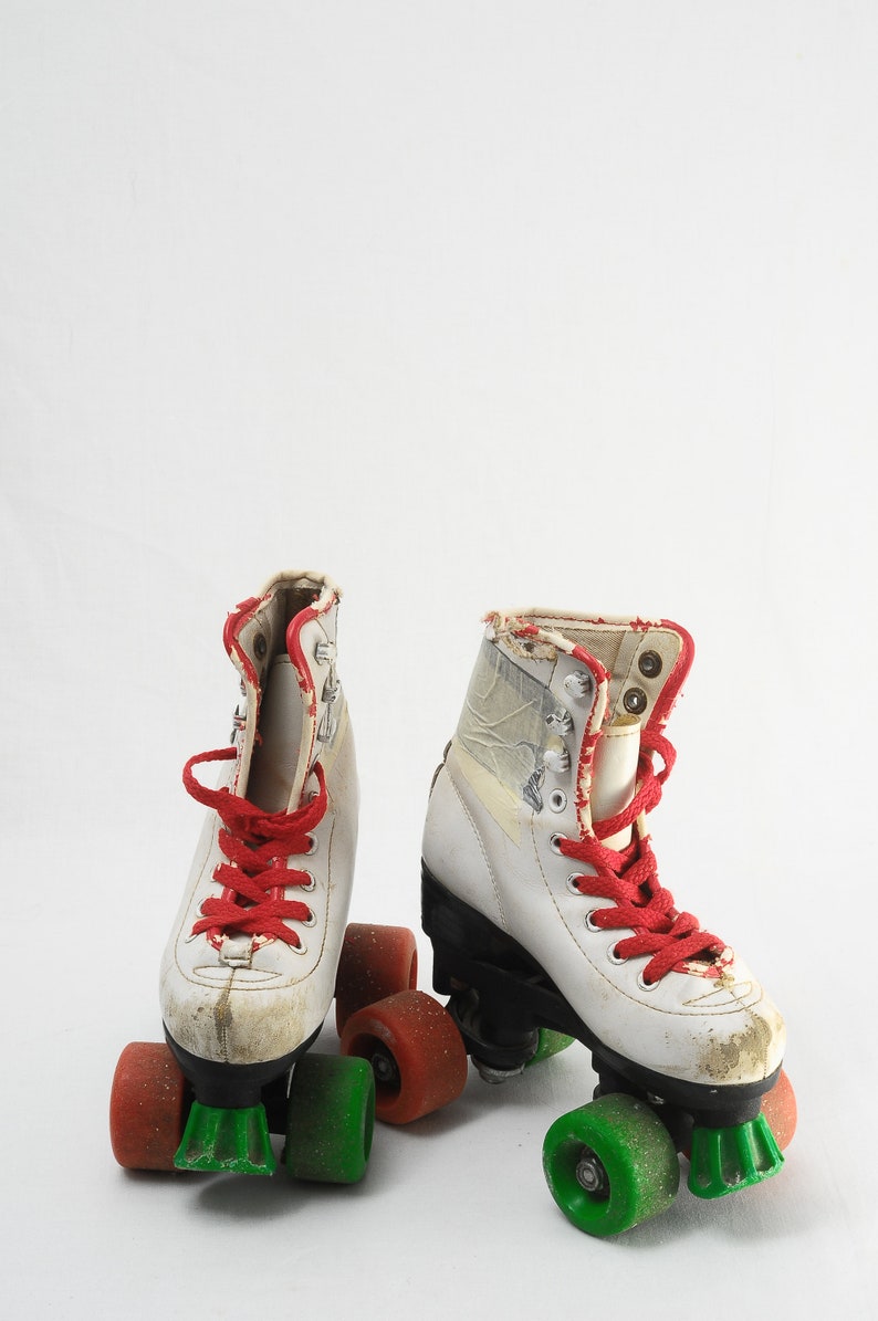 May include: A pair of white roller skates with red laces and green wheels. The skates have a worn look and are on a white background.