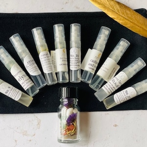 May include: A black pouch with a gold feather on top, containing ten small glass bottles with spray tops and a small glass bottle with a cork stopper. The bottles are labeled with names and numbers, such as "Aroma Elysi No. 9", "Aromal Stel No. 31", and "Cashmere and Vanilla".