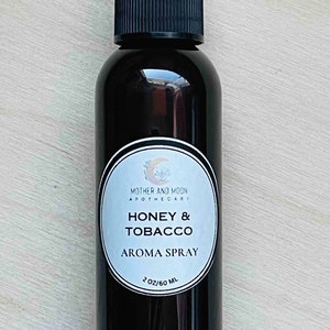 May include: A 60 ml brown glass bottle with a black spray top. The label is white with black text that reads "Mother and Moon Apothecary" and "Honey & Tobacco Aroma Spray".