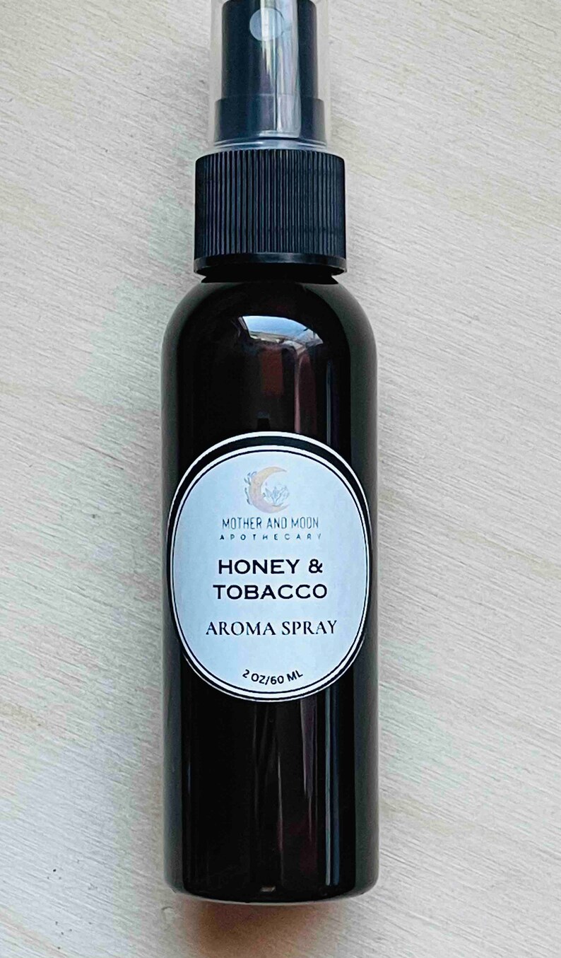 May include: A 60 ml brown glass bottle with a black spray top. The label is white with black text that reads "Mother and Moon Apothecary" and "Honey & Tobacco Aroma Spray".