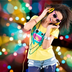 May include: A young woman with long brown hair is wearing yellow and blue clothing, pink sunglasses, and yellow headphones. She is smiling and listening to music. The background is a blur of colorful lights.
