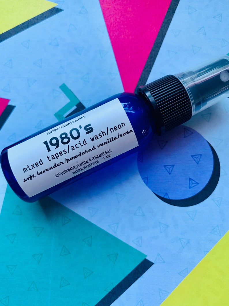 May include: A blue glass bottle with a black spray nozzle. The label reads "1980's mixed tapes/acid wash/neon soft lavender/powdered vanilla/rosc" and "motherandmoon.com".