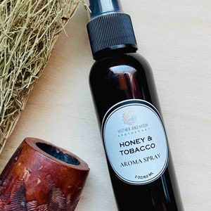 May include: A brown glass bottle with a black spray top and a white label that reads "Mother and Moon Apothecary Honey & Tobacco Aroma Spray 2 oz/60 ml".