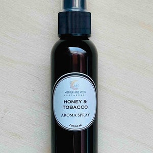May include: A 60 ml brown glass bottle with a black spray top. The label reads "Mother and Moon Apothecary" and "Honey & Tobacco Aroma Spray".