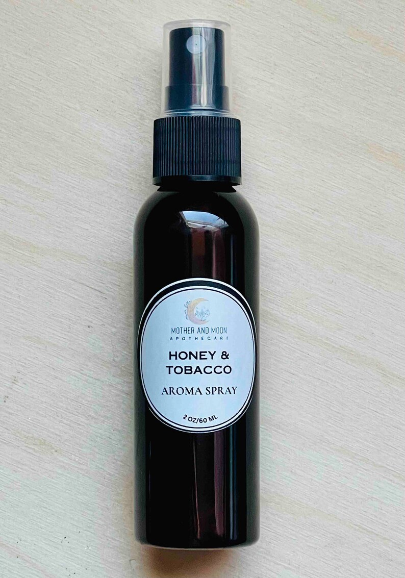 May include: A 60 ml brown glass bottle with a black spray top. The label reads "Mother and Moon Apothecary" and "Honey & Tobacco Aroma Spray".