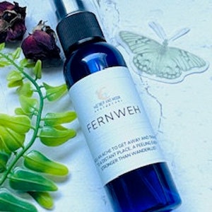 May include: A blue glass bottle with a spray nozzle, containing a clear liquid. The label reads "Fernweh" and includes the text "A longing to get away and see a distant place, a feeling stronger than wanderlust."