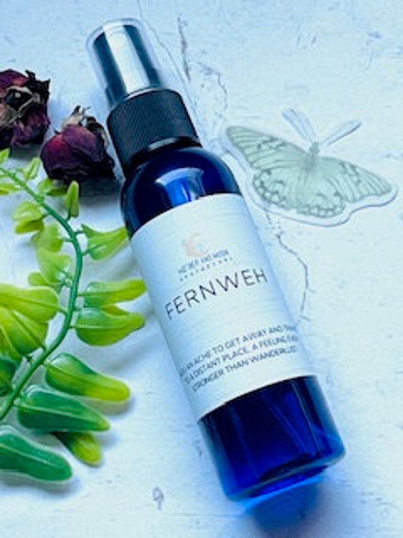 May include: A blue glass bottle with a spray nozzle, containing a clear liquid. The label reads "Fernweh" and includes the text "A longing to get away and see a distant place, a feeling stronger than wanderlust."