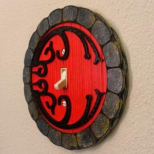 May include: A red door light switch cover with a black stone-like frame. The door has a decorative design and a white toggle switch.