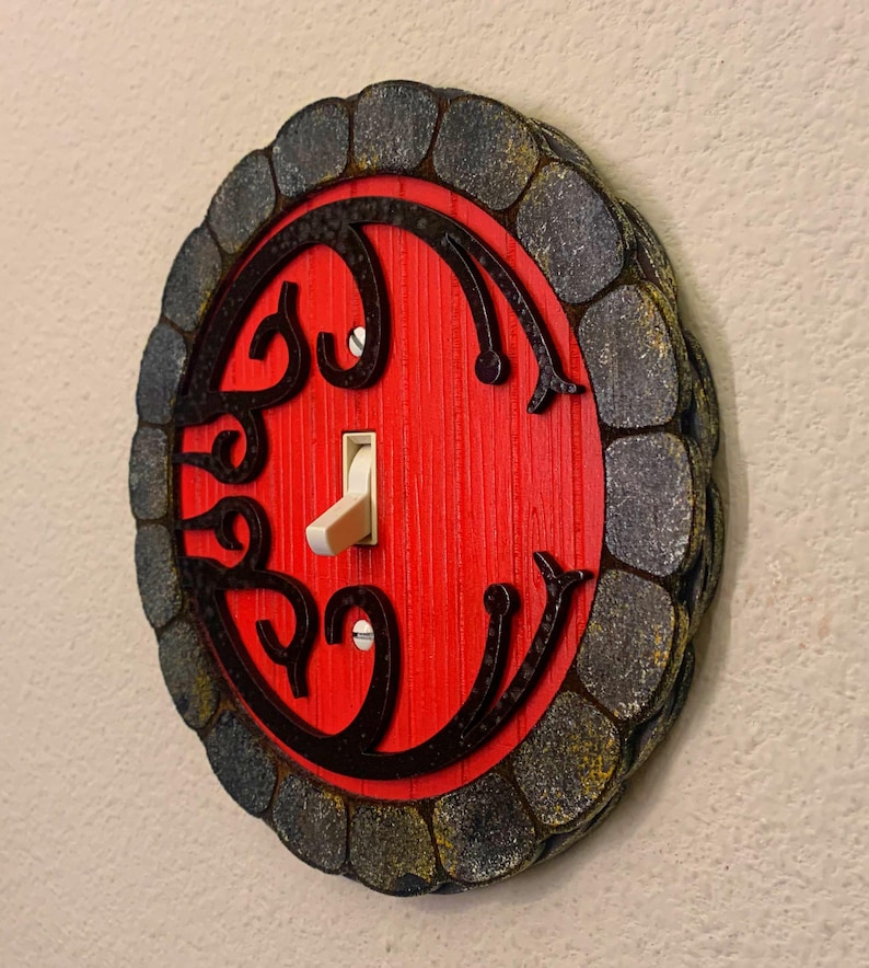 May include: A red door light switch cover with a black stone-like frame. The door has a decorative design and a white toggle switch.