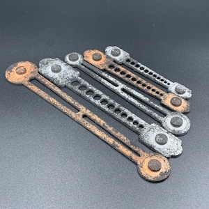 Peut inclure: Six sangles métalliques avec une finition usée et vieillie. Les sangles sont de différentes tailles et présentent un schéma de couleurs argent et orange. Les sangles ont une série de trous sur toute leur longueur et un bouton rond à chaque extrémité.
