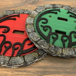 May include: Two decorative light switch covers with a stone-like border. One cover is red with black detailing and the other is green with black detailing.