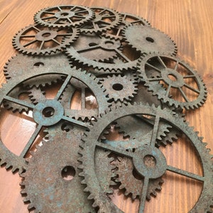 May include: A collection of rustic, metal gears in various sizes, with a distressed, aged finish. The gears are arranged in a random pattern, creating a visually interesting and textured design.