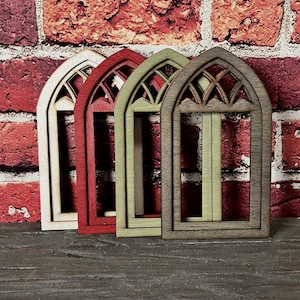 May include: Four arched wooden window frames featuring a decorative lattice design at the top. The frames are finished in natural light wood, deep red, sage green, and dark brown, arranged in a row with a vertical orientation and rectangular base.