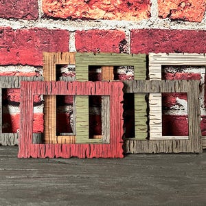 May include: A collection of rectangular picture frames featuring a textured wood grain pattern. The frames are finished in various colors including red, olive green, light beige, and grey, each with a distinct bark-like surface detail.