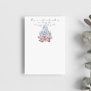 May include: White folded card with a watercolor illustration of a fairytale castle, surrounded by pink and peach flowers. The card has the text: "Once in a while, in the middle of an ordinary life... love gives us a fairy tale."