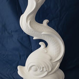 May include: A white dolphin sculpture with a curved, flowing design. The sculpture has a textured surface and is set against a dark blue background. The dolphin is depicted in a dynamic pose, with its tail and body curving upwards.