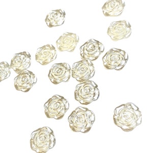 May include: A collection of small, translucent rose-shaped embellishments. The clear, slightly iridescent flowers are scattered against a white background. These decorative elements are ideal for crafts and DIY projects.