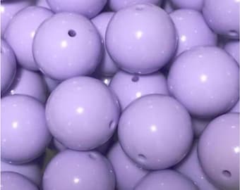 May include: A collection of light purple, round beads with a glossy finish. Each bead has a small hole, suggesting they are for stringing. The beads are clustered together, filling the frame, and are likely for jewelry making or crafts.