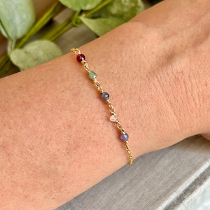 May include: A delicate gold chain bracelet adorned with a series of colorful gemstones. The bracelet features a mix of red, green, blue, and clear stones, creating a vibrant and elegant accessory.