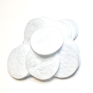 May include: A collection of white, round, cotton pads. The pads are stacked and slightly overlapping, with a soft, textured appearance. They are arranged against a bright white background, creating a clean and simple aesthetic.