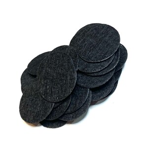 May include: A collection of small, black, oval-shaped felt pads. The pads are arranged in a cluster, with a textured surface. The background is plain white, providing a contrast to the dark color of the felt.