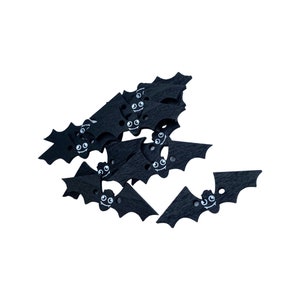 May include: A collection of black wooden bat-shaped decorations with white painted eyes and smiles. These Halloween-themed bats are arranged in a pile, with some scattered around. The bats have a textured surface.