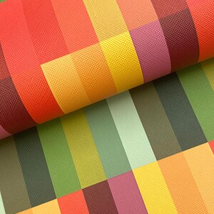 May include: Close-up of a colorful fabric with a geometric pattern. The design features vertical and horizontal stripes in shades of red, orange, yellow, green, and purple. The fabric is folded, revealing the texture and depth of the material.