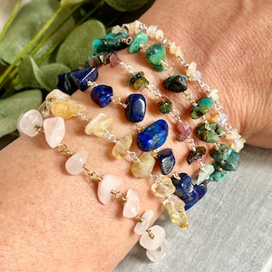 Peut inclure: Plusieurs bracelets de pierres précieuses avec diverses pierres colorées. Les bracelets comprennent du quartz rose, de la citrine, du lapis-lazuli et de la turquoise, enfilés avec du fil doré. Les bracelets sont portés au poignet.
