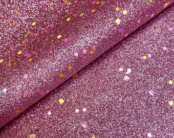 May include: Close-up of a textured, glittery fabric in a deep rose color. The fabric is sprinkled with small, colorful confetti-like shapes in shades of yellow, pink, and green. The fabric is folded over, revealing its texture and sheen.