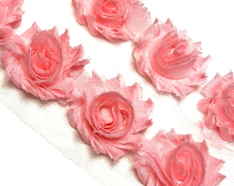 May include: Close-up of a delicate pink rose trim. The trim features multiple fabric roses with ruffled edges, attached to a sheer white mesh backing. The roses are a soft, pastel pink color, perfect for crafting and embellishments.