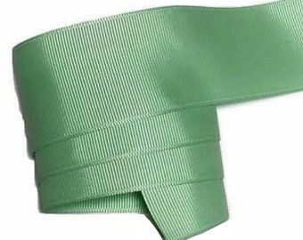 May include: A roll of sage green grosgrain ribbon. The ribbon has a ribbed texture and is folded over itself. The color is a soft, muted green, and the ribbon appears to be made of a sturdy material, suitable for crafts and embellishments.
