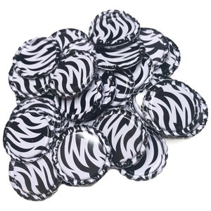 May include: A pile of bottle caps with a black and white zebra stripe pattern. The caps are round with a crimped edge and a glossy finish. The caps are scattered on a white background.