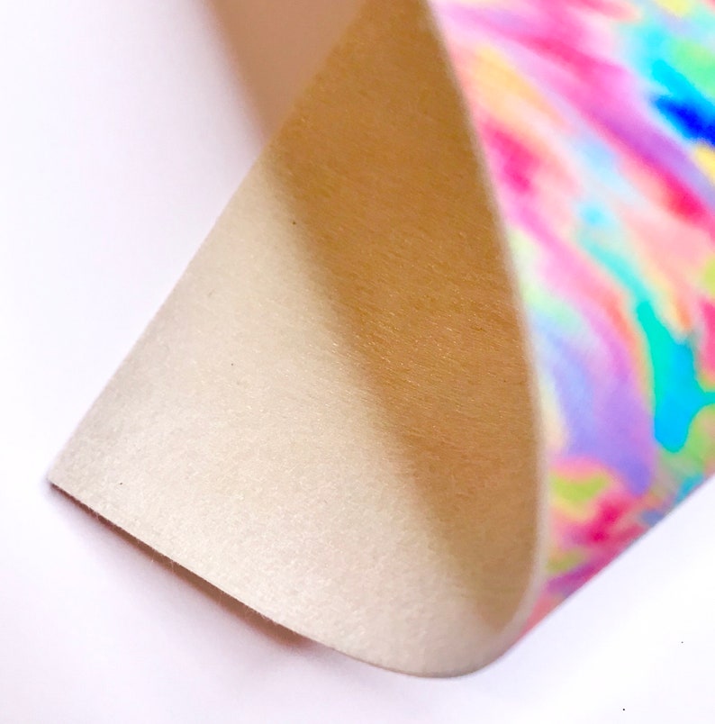 May include: A close-up of a piece of fabric with a tie-dye pattern in shades of pink, blue, green, and yellow. The fabric is folded over, revealing a white, fuzzy underside.