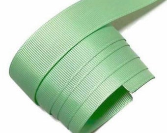 May include: A roll of light green grosgrain ribbon. The ribbon is a solid color with a ribbed texture. The ribbon is rolled up, showing the edges and the texture of the fabric. The background is white.