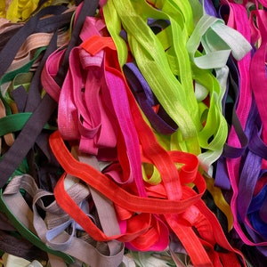 Puede incluir: Un mont&oacute;n grande de cintas el&aacute;sticas para el pelo de colores en varios tonos de rosa, verde, azul, naranja y gris.