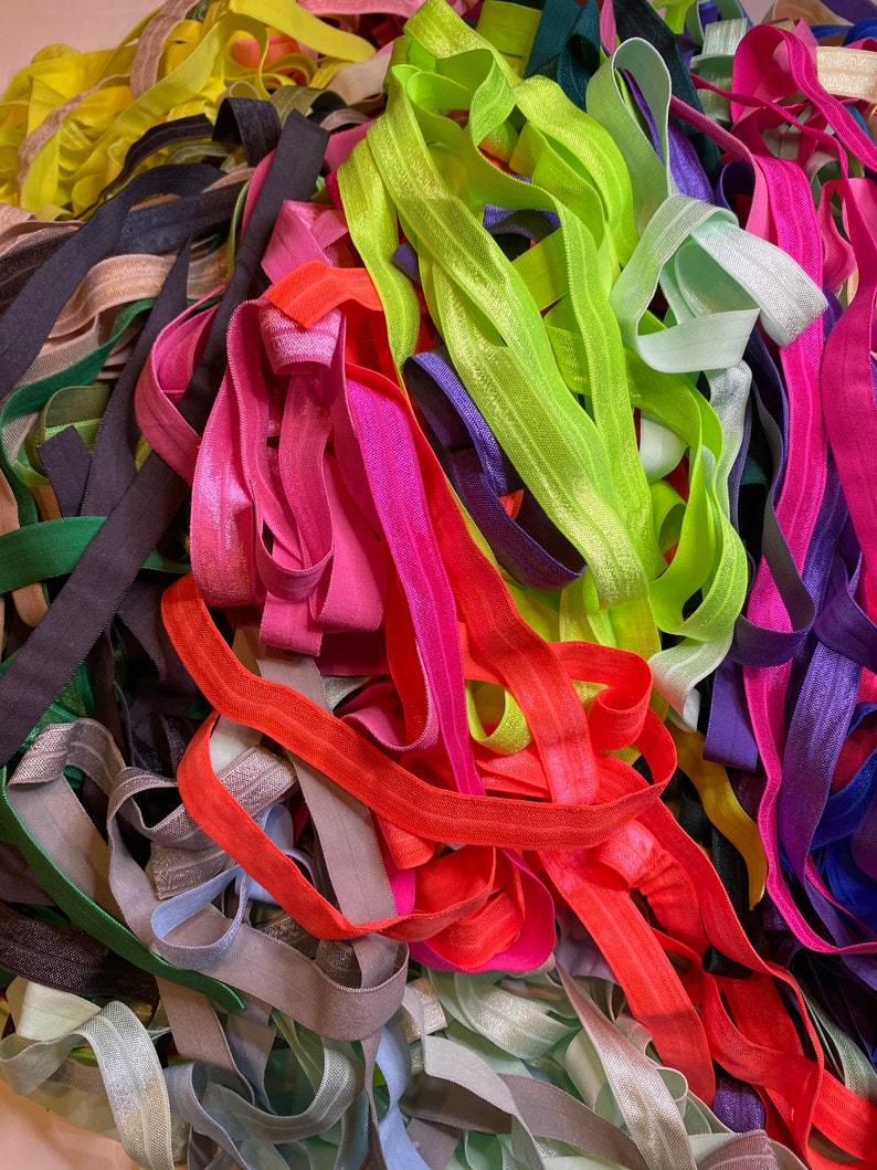 Puede incluir: Un mont&oacute;n grande de cintas el&aacute;sticas para el pelo de colores en varios tonos de rosa, verde, azul, naranja y gris.