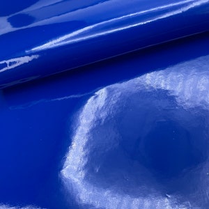May include: A close-up shot of a sheet of glossy, royal blue vinyl fabric. The surface reflects light, creating highlights and shadows that emphasize the texture and sheen of the material. The fabric appears smooth and durable.