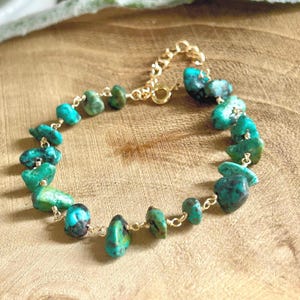 Peut inclure: Bracelet en chaîne dorée orné de pierres de turquoise irrégulières. Les pierres, de teintes turquoise, sont reliées par de petites chaînes dorées. Le bracelet est doté d'un fermoir mousqueton. Les pierres mesurent environ 0,5 à 1 cm.