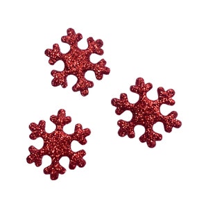 May include: Three red glitter snowflake ornaments against a white background. Each snowflake has six points and a textured, sparkling surface. These decorative accents are ideal for holiday crafts and winter-themed decor.