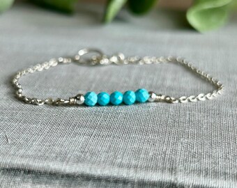 May include: A delicate silver bracelet featuring a series of six vibrant turquoise beads. The bracelet has a fine chain design and a secure clasp. The turquoise beads are the focal point, adding a pop of color.