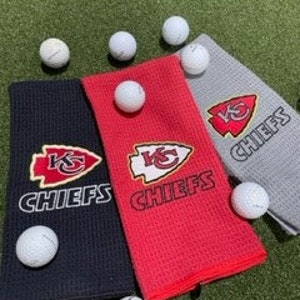 May include: Three golf towels with the Kansas City Chiefs logo. The towels are black, red, and gray.