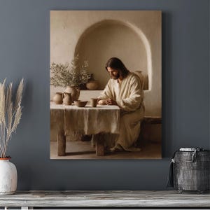 May include: A wall art print depicting a person with long brown hair and a beard, wearing a light-colored robe, sitting at a wooden table. On the table are several ceramic vessels, a small bowl, and a cup. The scene is set in a room with an arched wall niche, rendered in neutral beige and brown tones.