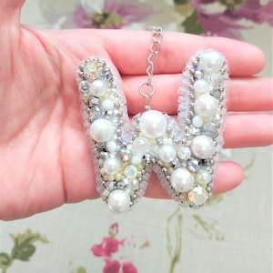 May include: A white letter W charm made of pearls and rhinestones. The charm is attached to a silver chain.