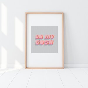 Op de afbeelding: Een ingelijste print met de tekst "OH MY GOSH" in roze en oranje 3D-letters. De tekst staat tegen een grijze achtergrond met patroon. De lijst is licht van kleur en de print wordt op een witte muur getoond.