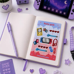 Op de afbeelding: Een stickervel met de titel Game geek met illustraties van een gele handheld console, spelcartridges, rode harten, een blauwe stylus, een rood-blauwe handheld console, een rode koptelefoon en controllers, met de tekst LaviluneDoodles onderaan.